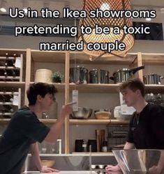 two men are talking to each other in front of a shelf full of pots and pans