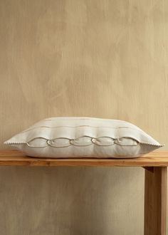 a white pillow sitting on top of a wooden table next to a wall with no one in it