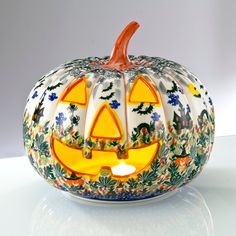 a glass pumpkin with an illuminated face on it's side, sitting on a table