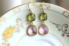 two pairs of pink and green earrings sitting on top of a white plate with gold trimming