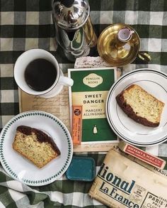 a table topped with plates and cups filled with food next to an old book, tea pot