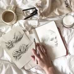 a person's hand holding a pencil next to two drawings on top of a bed