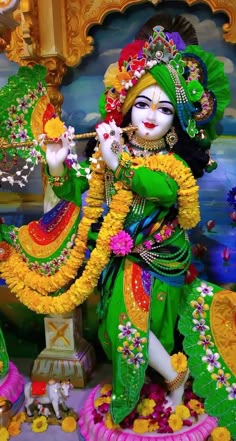 a statue of a hindu god in front of a colorful wall with flowers and decorations