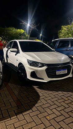 two white cars parked next to each other in a parking lot at night with lights on