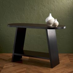 two white vases sitting on top of a wooden table next to a green wall