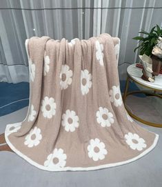 a blanket with white flowers on it is sitting next to a table and potted plant