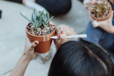 a woman holding up a potted plant with small rocks in it and a pencil