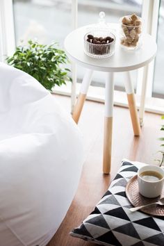 a white table topped with a cup of coffee next to a potted plant on top of a wooden floor