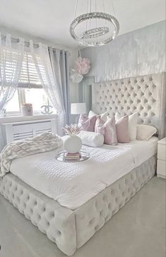 a white bed sitting in a bedroom next to a window covered in curtains and pillows