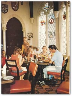 a group of people sitting around a table in a room with stained glass windows on the walls