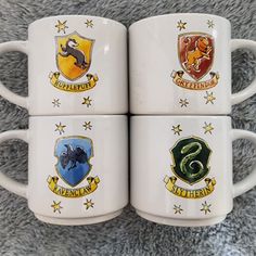 four harry potter coffee mugs with hogwart and sly emblems on the sides