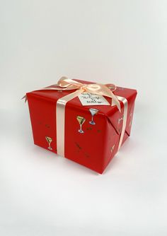 a red gift box wrapped in gold ribbon and decorated with champagne glasses, is sitting on a white surface