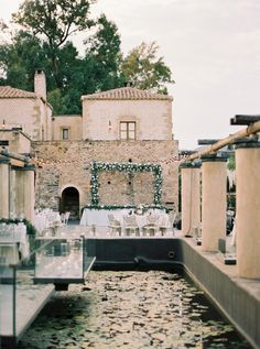 tables and chairs are set up in front of an old brick building with water running through it