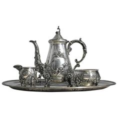 an ornate silver tea set with four cups and two saucers on a metal tray