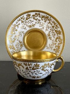 a white and gold cup with saucer sitting on top of a black countertop