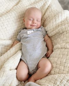 a baby laying on top of a bed covered in a white and gray blanket with his eyes closed