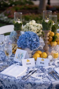 the table is set up with blue and white flowers, lemons, and candles