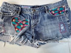 a pair of cut off shorts with embroidered hearts on the front and back pockets, sitting on a white surface