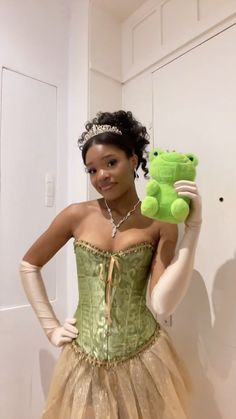 a woman in a dress holding a green teddy bear wearing a tiara and gloves