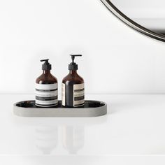 two bottles of soap sit on a tray in front of a mirror