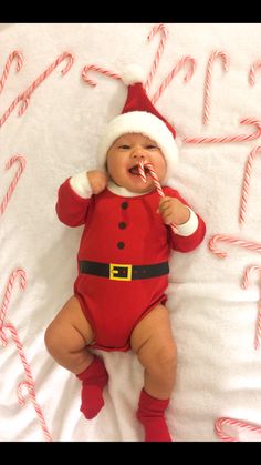 a baby wearing a santa suit and holding a candy cane in it's mouth