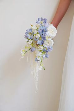 a bride's bouquet with blue and white flowers is being held by her hand