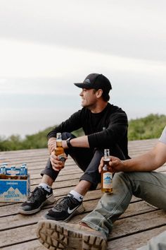 two men sitting on a wooden deck with bottles of beer in front of their feet