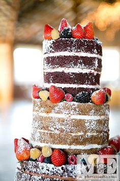 a multi layer cake sitting on top of a table covered in berries and powdered sugar