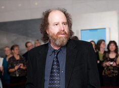 a man with a beard wearing a suit and tie standing in front of a group of people