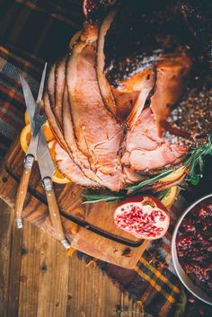 sliced ham with cranberry sauce on cutting board next to knife and bowl of fruit