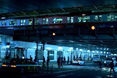 people are crossing the street at night in front of a train station with lights on