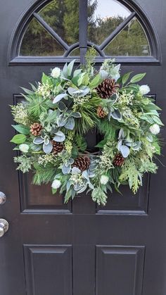 a wreath with pine cones and greenery hangs on the front door's black door