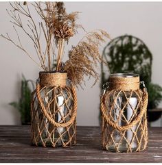 two glass jars with plants in them sitting on a table