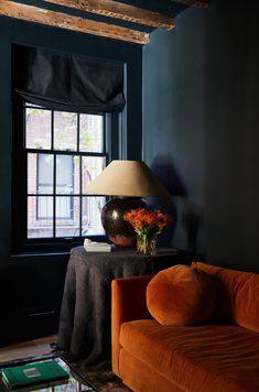 an orange couch sitting in front of a window next to a table with a lamp on it