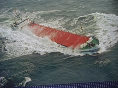 a large red and green boat in the middle of some choppy ocean water with waves