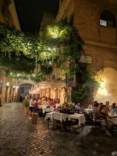 people sitting at tables in an alleyway with trees growing on the side of it