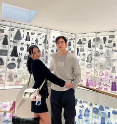 a man and woman standing next to each other in front of a wall full of handbags