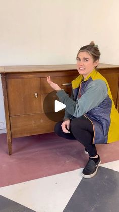 a woman sitting on the floor in front of a wooden cabinet and pointing at something