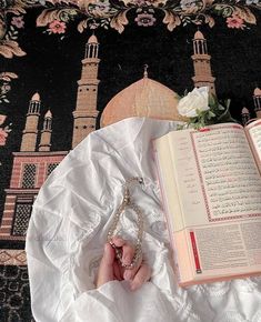 an open book on top of a table next to a rosary and flower potted plant