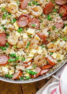 a pan filled with rice, peas and sausages on top of a wooden table