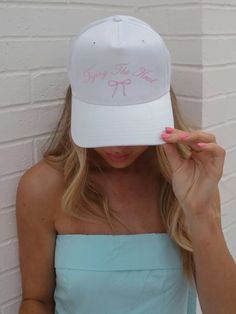 a woman wearing a white hat with pink writing on the front and back, covering her eyes