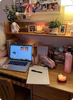 an open laptop computer sitting on top of a wooden desk next to a lit candle