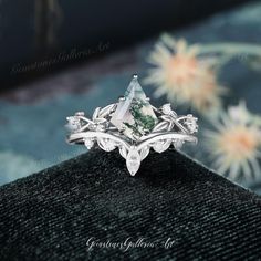 a close up view of an engagement ring with a green stone and leaves on it