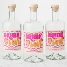 three bottles of drunk love vodka on a marble countertop with pink and yellow labels