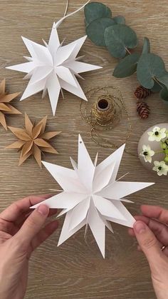 two hands holding white paper stars on top of a wooden table next to greenery