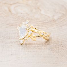 a gold ring with a pear shaped stone surrounded by small white diamonds on a wooden surface