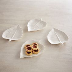 three white plates with leaves on them sitting on a table next to some cookies and fruit