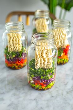 four mason jars filled with noodles and vegetables