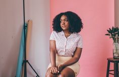 a woman sitting on top of a stool next to a pink wall