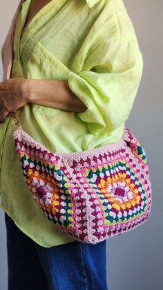 a woman is holding a crocheted bag in her hands and wearing a green shirt